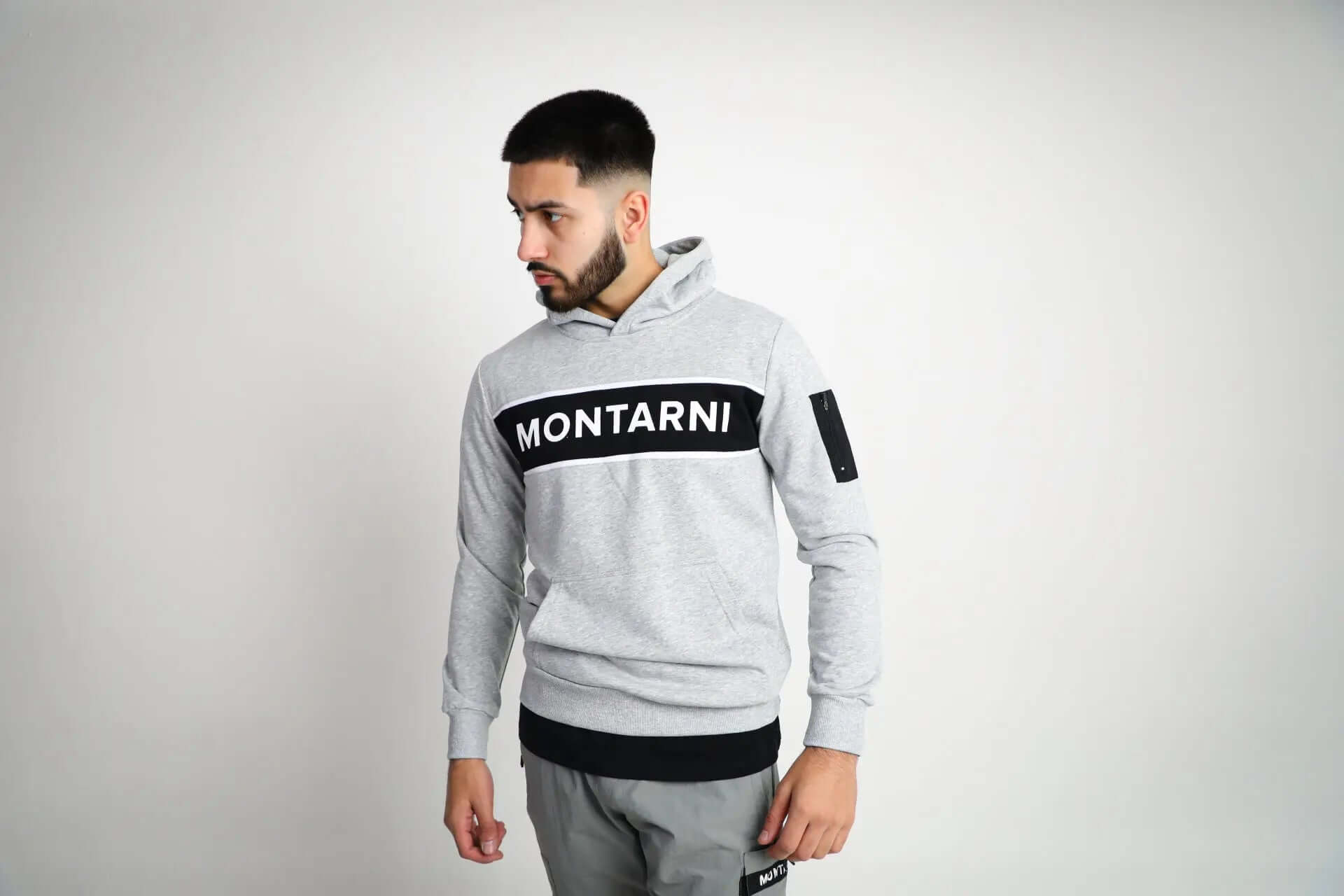 Model wearing Montarni grey gym hoodie men with long sleeves, kangaroo pocket and sporty tape stripe branding