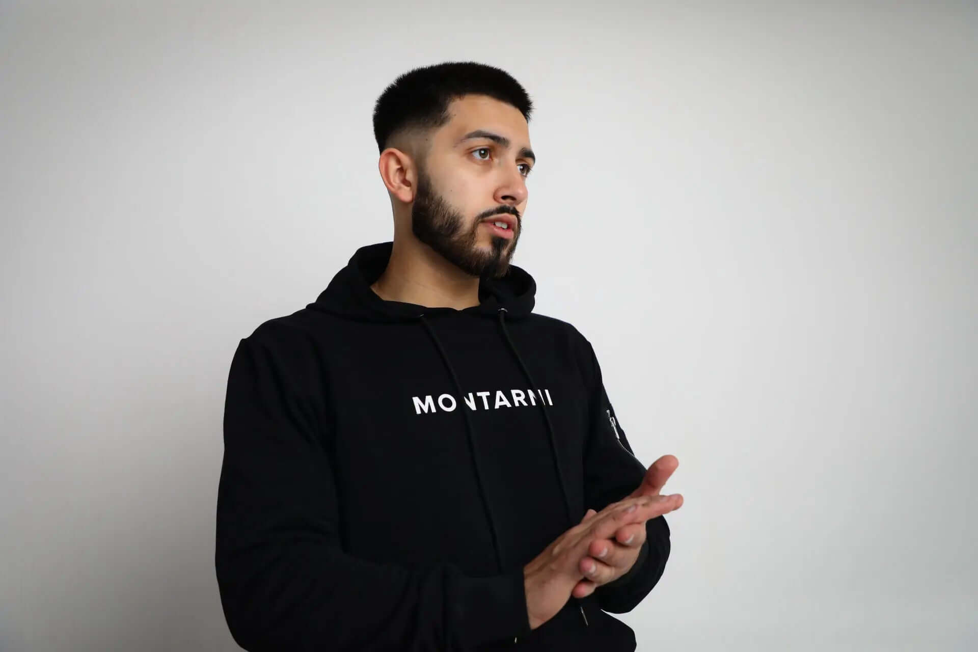 Side view of Montarni black tech hoodie showing left-arm zip pocket and ribbed hem