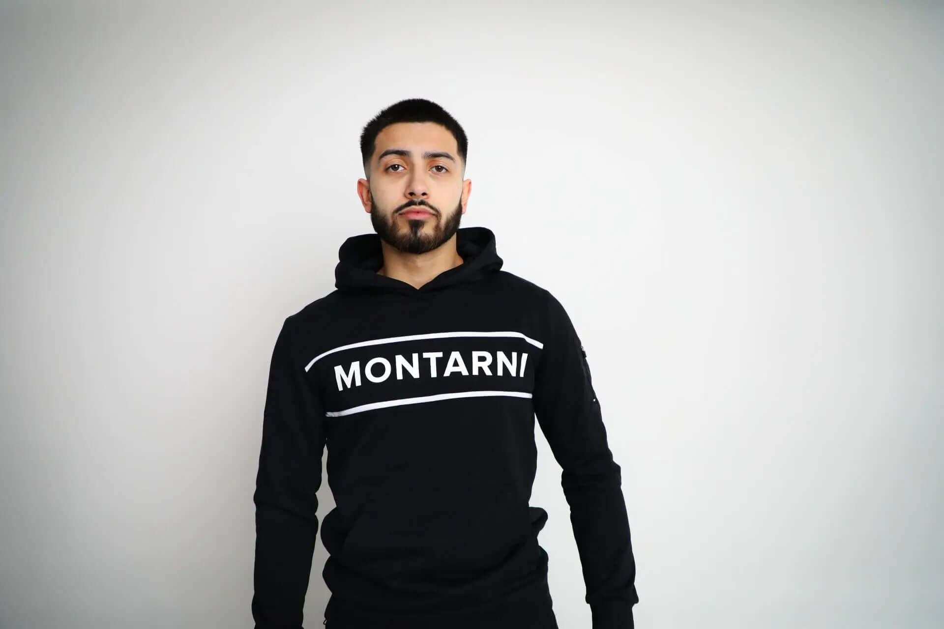 Model wearing Montarni black gym hoodie men with long sleeves, kangaroo pocket and sporty tape stripe branding