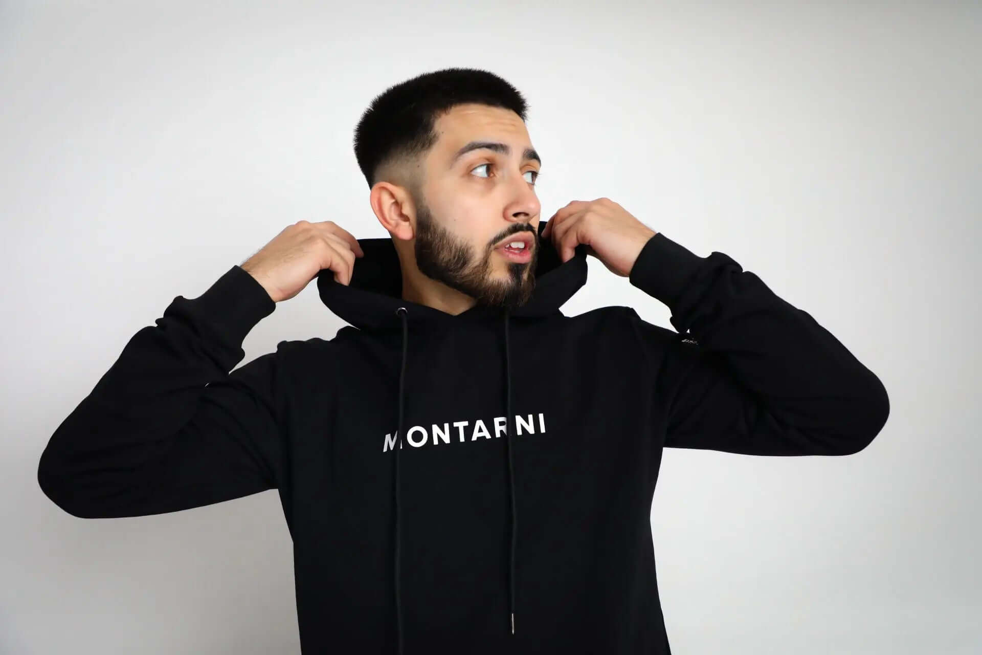 Male model wearing Montarni black tech hoodie with adjustable hood, kangaroo pocket, and arm zip pocket
