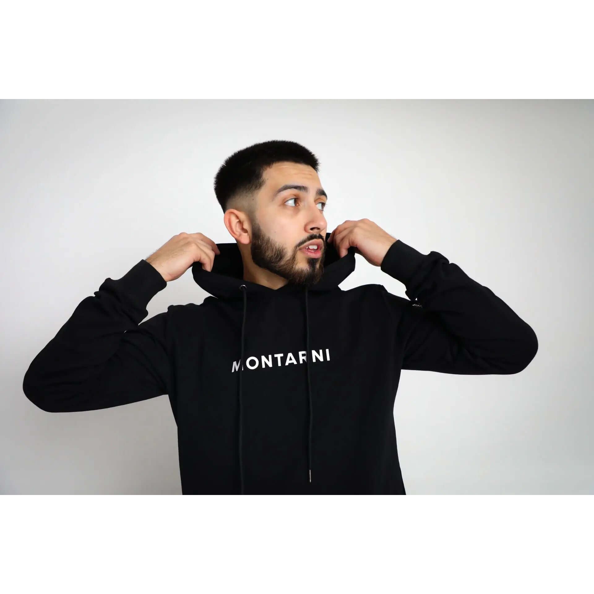 Man adjusting hoodie featuring Montarni logo, wearing a stylish Techwear hoodie designed for performance and fashion.