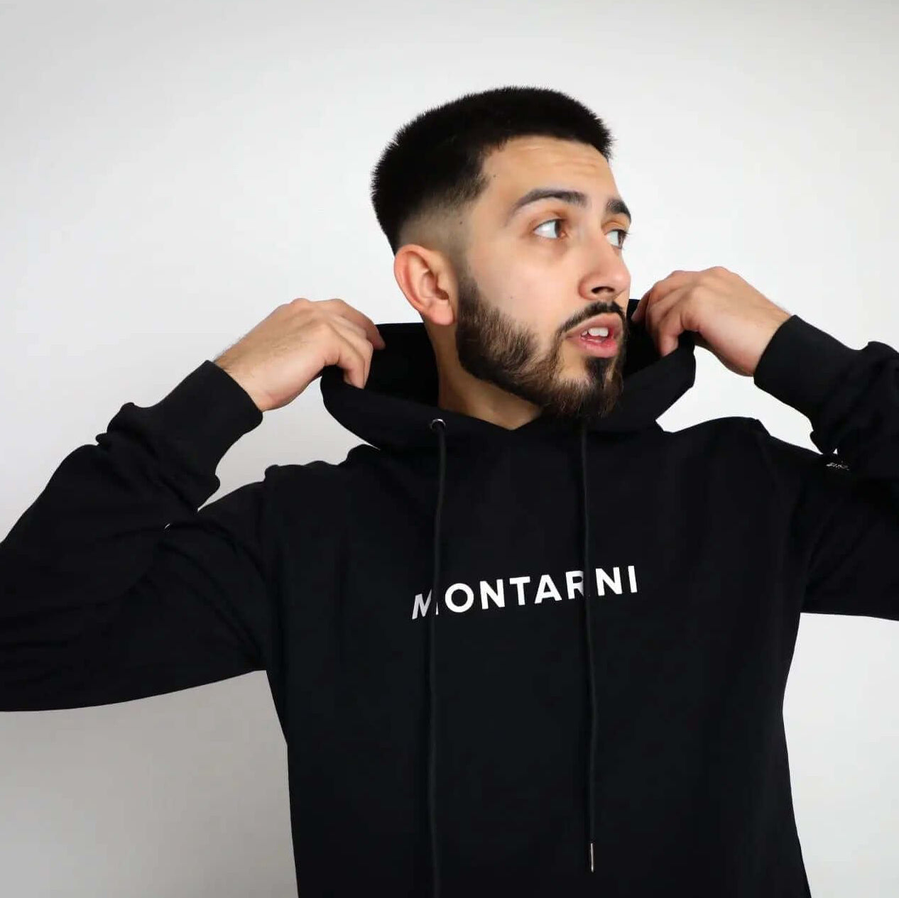 Man adjusting hoodie featuring Montarni logo, wearing a stylish Techwear hoodie designed for performance and fashion.